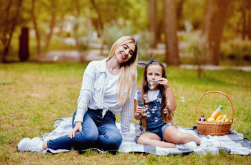 Fototapeta premium Weekend With Mom. Little Girl And Her Mother Blowing Soap Bubbles Having Fun On Picnic In City Park Outside