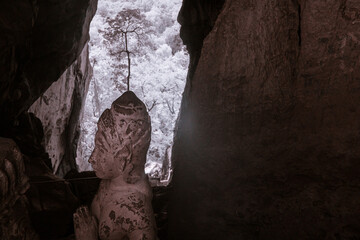 Infrared color, a Buddha or a similar figure situated in a rocky, cave-like environment