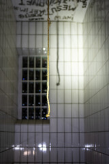 A lone rope hangs in a dimly lit, tile-walled room with graffiti on the ceiling, near a barred window.