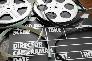 Movie clapper and film reels on wooden table, closeup