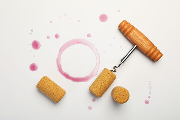 Corkscrew, corks and red wine stains on white background, top view
