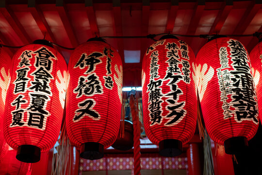 Illuminated red Japanese lanterns with elegant black calligraphy hang festively under a red ceiling.