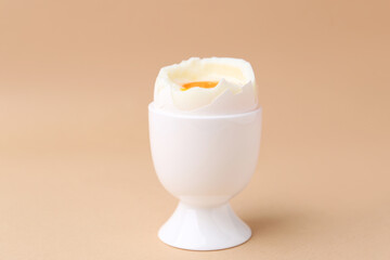 Soft boiled egg in cup on beige background, closeup