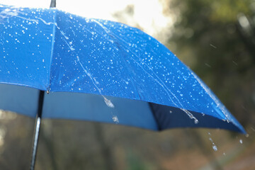Open blue umbrella under pouring rain outdoors, closeup