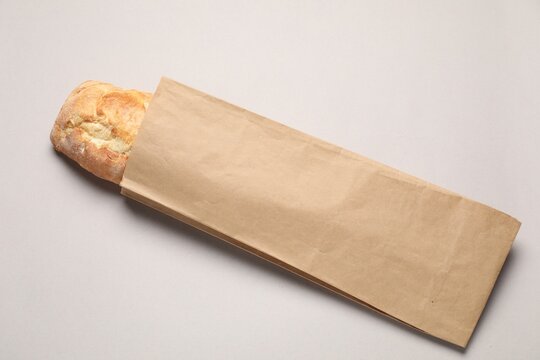 Paper bag with fresh baguette on light gray table, top view