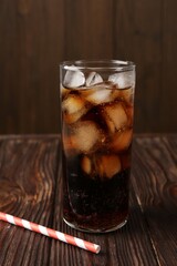 Cold cola with ice cubes in glass and drinking straw on wooden table