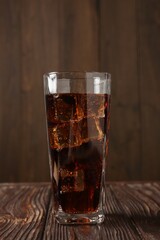 Cold cola with ice cubes in glass on wooden table