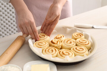 Woman making cinnamon rolls at white wooden table, closeup