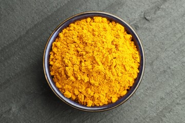 Turmeric powder in bowl on grey table, top view