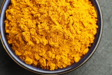 Turmeric powder in bowl on grey table, closeup. Top view