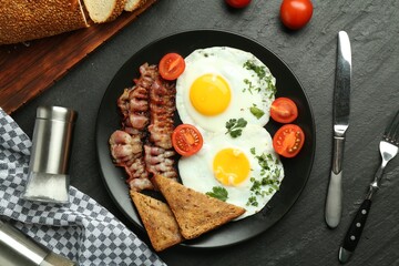 Tasty brunch. Delicious fried eggs, bacon and pieces of toast served on black table, flat lay