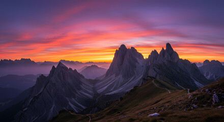 Sunset behind rugged mountain peaks, casting an orange and purple glow across the sky, with shadows stretching across the rolling landscape