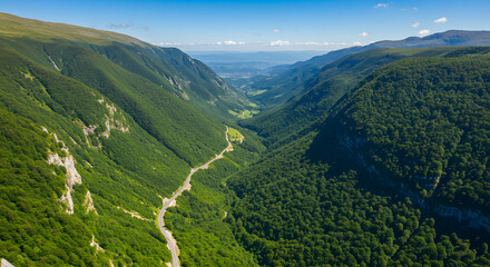 Obraz premium Lush green valleys nestled between steep mountain slopes, with a winding road cutting through the landscape under a bright sky