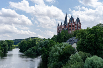 Obraz premium Serene summer view: A majestic cathedral stands tall amidst vibrant greenery, overlooking a calm river.