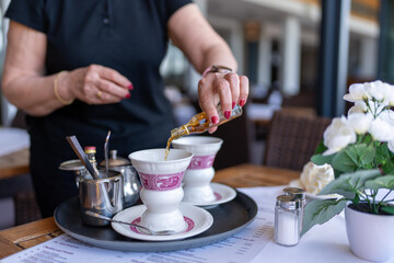 Waitress pouring flavored syrup into a traditional coffee cup at an outdoor cafe, adding a touch of sweetness.