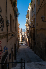 Obraz premium Sunlit alleyway between aged buildings opens to a vibrant cityscape with a Ferris wheel in the distance.