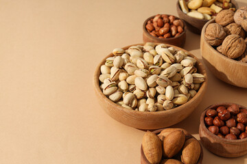 Various nuts in wooden bowls on a beige background