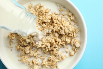 Pouring milk into bowl with oatmeal at light blue table, top view