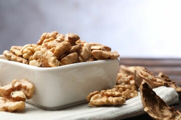 Peeled walnuts in bowl on table against light background, closeup. Space for text