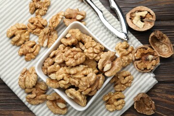 Peeled walnuts in bowl and nutcracker on wooden table, flat lay