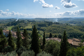 Obraz premium A picturesque Tuscan landscape unfolds, showcasing rolling hills dotted with cypress trees and charming villages under a partly cloudy sky.
