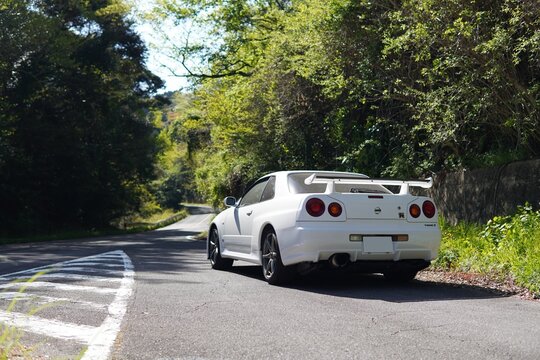 三重、日本 - 2021年4月11日 : ホワイトカラーの日産R34型スカイラインGT-R Vspec II、ワインディングロード、リアビュー