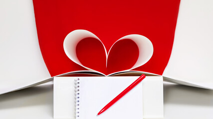 Red paper heart made from book pages on red background with pen and notebook
