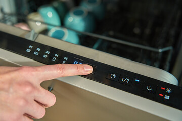 Close-up of female finger pressing button on dishwasher control panel. Woman using dishwasher in...