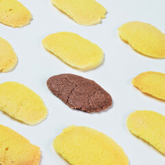 Indonesian lidah kucing. A striking layout features several yellow cookies surrounding a single brown cookie on a plain white backdrop, showcasing their contrast