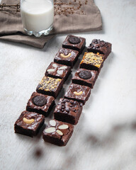 An assortment of chocolate brownies topped with nuts and cookies, arranged neatly beside a refreshing glass of milk