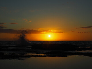 beautiful sunrise over the horizon at Tamarama beach in sydney, australia with a wave splashing against the rocks