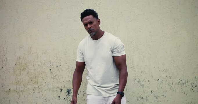 Man of African descent standing against textured wall, pointing forward with serious expression, confident and assertive body language, confrontational stance, strong presence