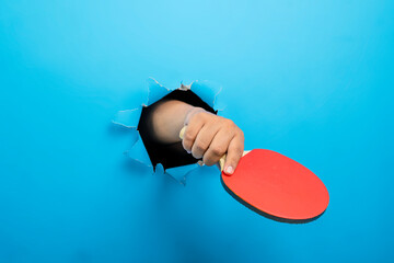 Human hand holding table tennis paddle through ripped paper. Mockup or Copy space. Concept of sport