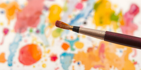 Obraz premium A fine brush tip dipped in bright watercolor, poised above a half-finished, colorful painting