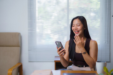 Asian businesswoman using smartphone and laughing during video call in office