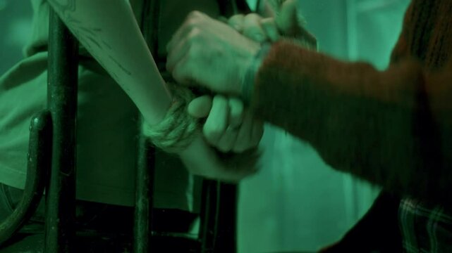 Close-up view of unrecognizable serial killer tying up hands of helpless victim trapped in dark basement. Thriller movie scene