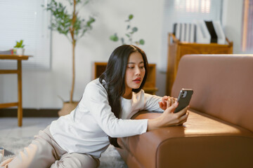 Obraz premium Young woman using smartphone while lying on floor in living room