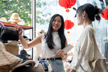 A smiling Asian shop employee is recommending new items to a customer, helping them select items.