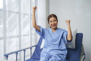Happy patient raising arms celebrating recovery sitting on bed in hospital room