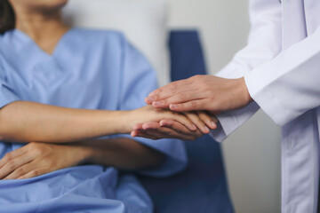 Doctor comforting patient by holding hands in hospital room
