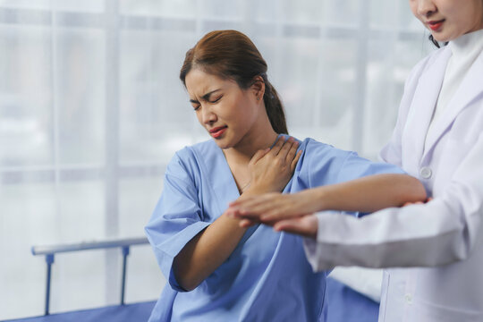 Doctor assisting patient suffering from shoulder and neck pain in hospital room