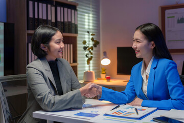 Two happy businesswomen shaking hands after closing a deal in office at night