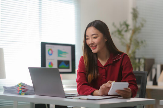 Asian businesswoman using calculator and working on laptop at modern office - Powered by Adobe