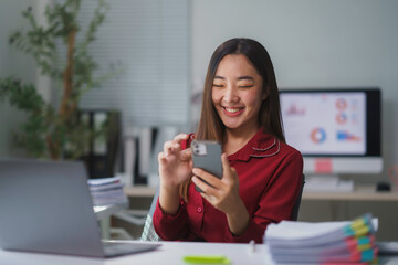 Asian businesswoman smiling and using smartphone in modern office