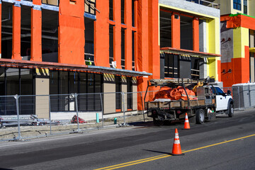 New multistory mixed use commercial and residential building under construction on a sunny winter day, orange building wrap and heavy work truck loaded with tarps
