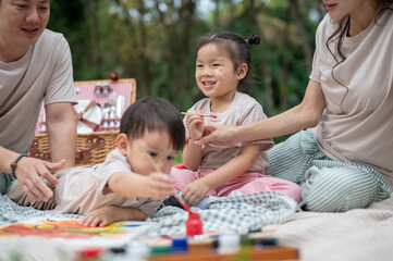 Obraz premium A cute little Asian boy enjoys coloring on a canvas while picnicking with his parents and sister.