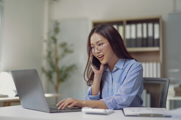 Young businesswoman talking on phone and working on laptop in office