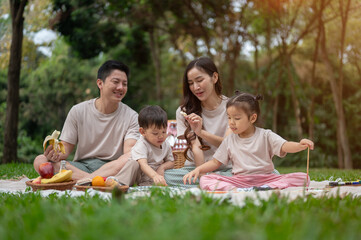 A cheerful Asian family enjoys a picnic in a park, playing with their little boy and girl.