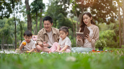 Fototapeta premium A joyful Asian family picnics in a park, enjoying a conversation and eating snacks.
