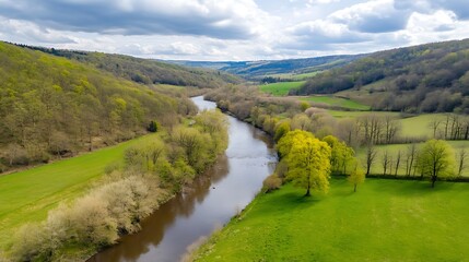 Obraz premium Serene River Valley Landscape: A Breathtaking Aerial View of Lush Green Meadows, Winding River, and Rolling Hills Under a Cloudy Sky